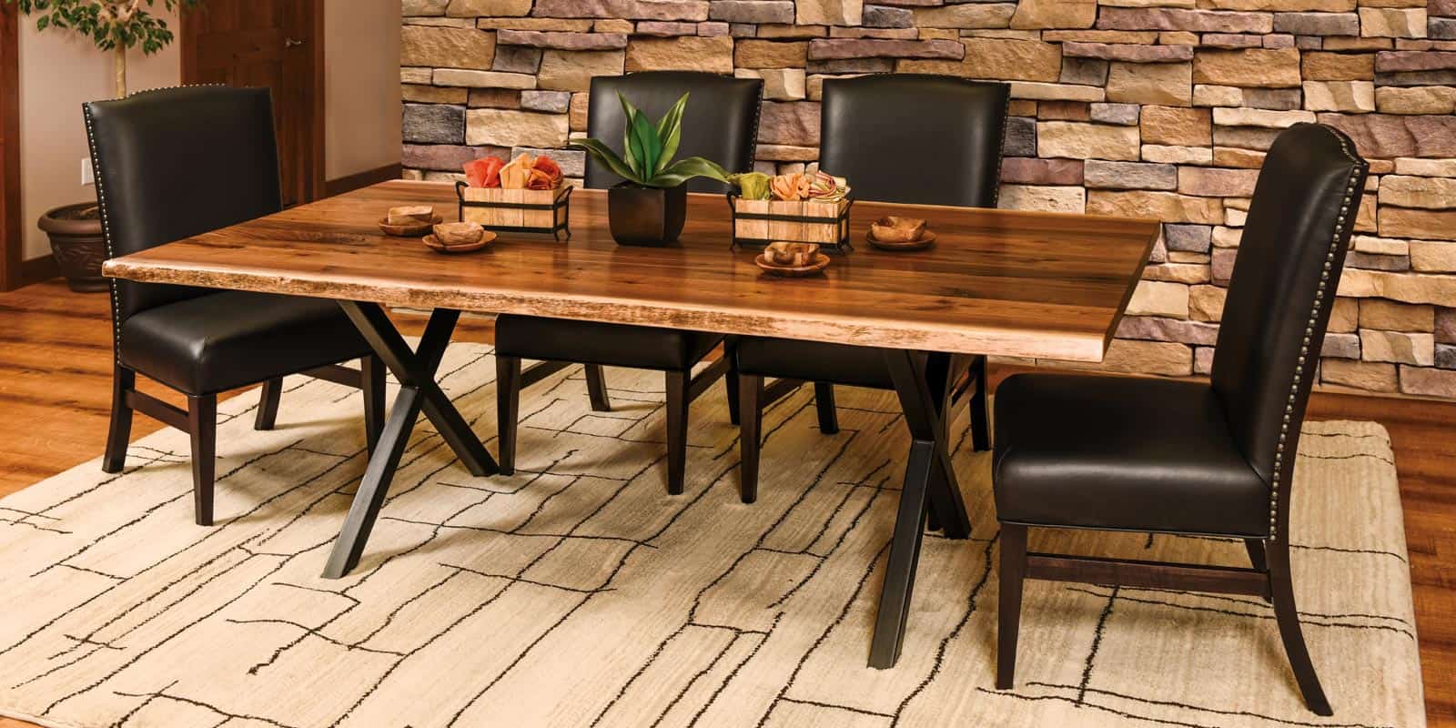 A live edge wood dining table with black metal x-shaped legs with 4 black leather chairs.